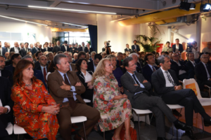 Platea di invitati all'inaugurazione de Le Village Sicilia in ottobre 2024 che assistono ai discorsi di apertura seduti ne La Place, lo spazio multimediale di 400 metri quadrati per eventi aziendali e conferenze